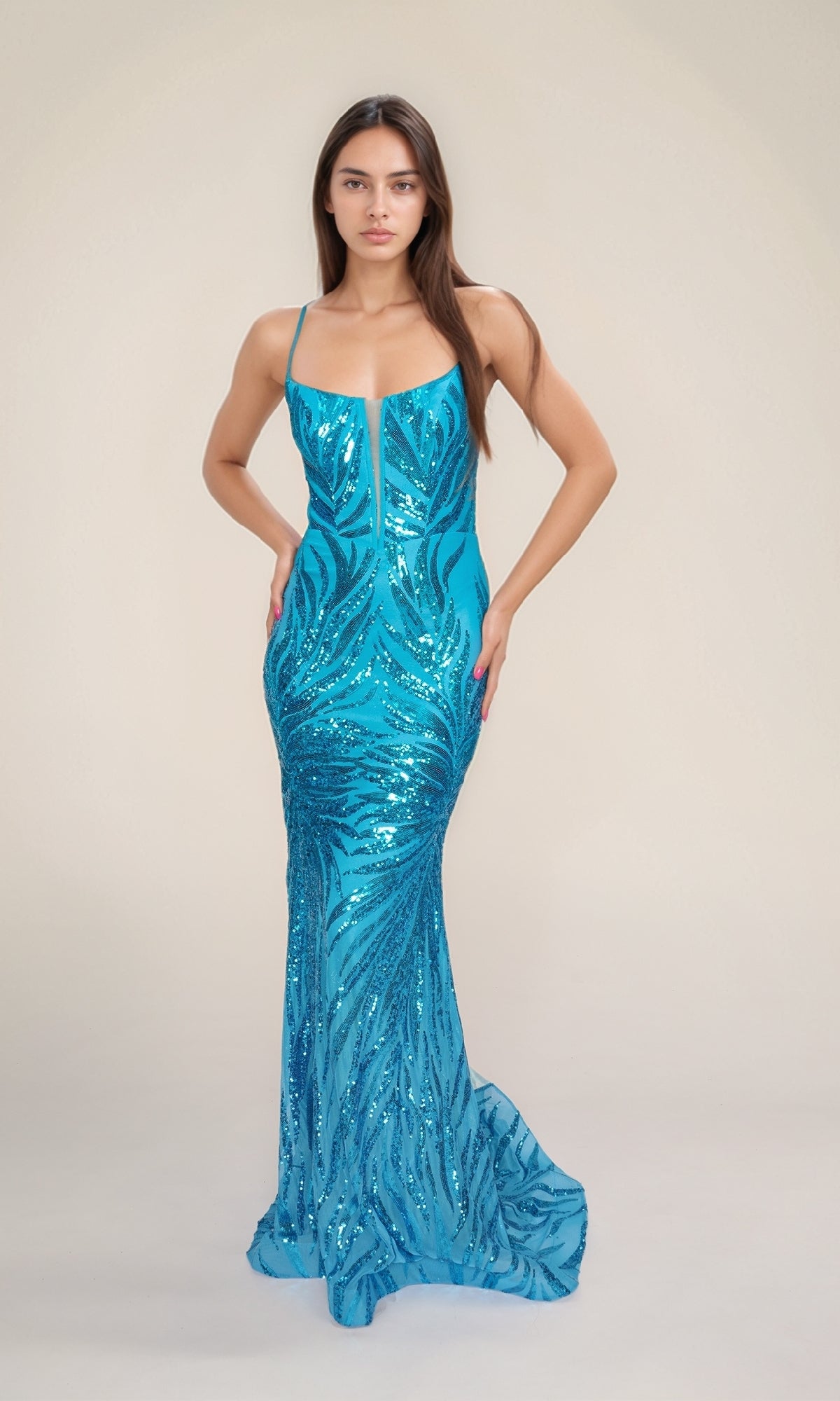A woman faces forward in the Nina Canacci 4433, a fitted, sleeveless blue sequin prom dress with thin straps, lace-up open back, and subtle leaf pattern, set against a plain light background.